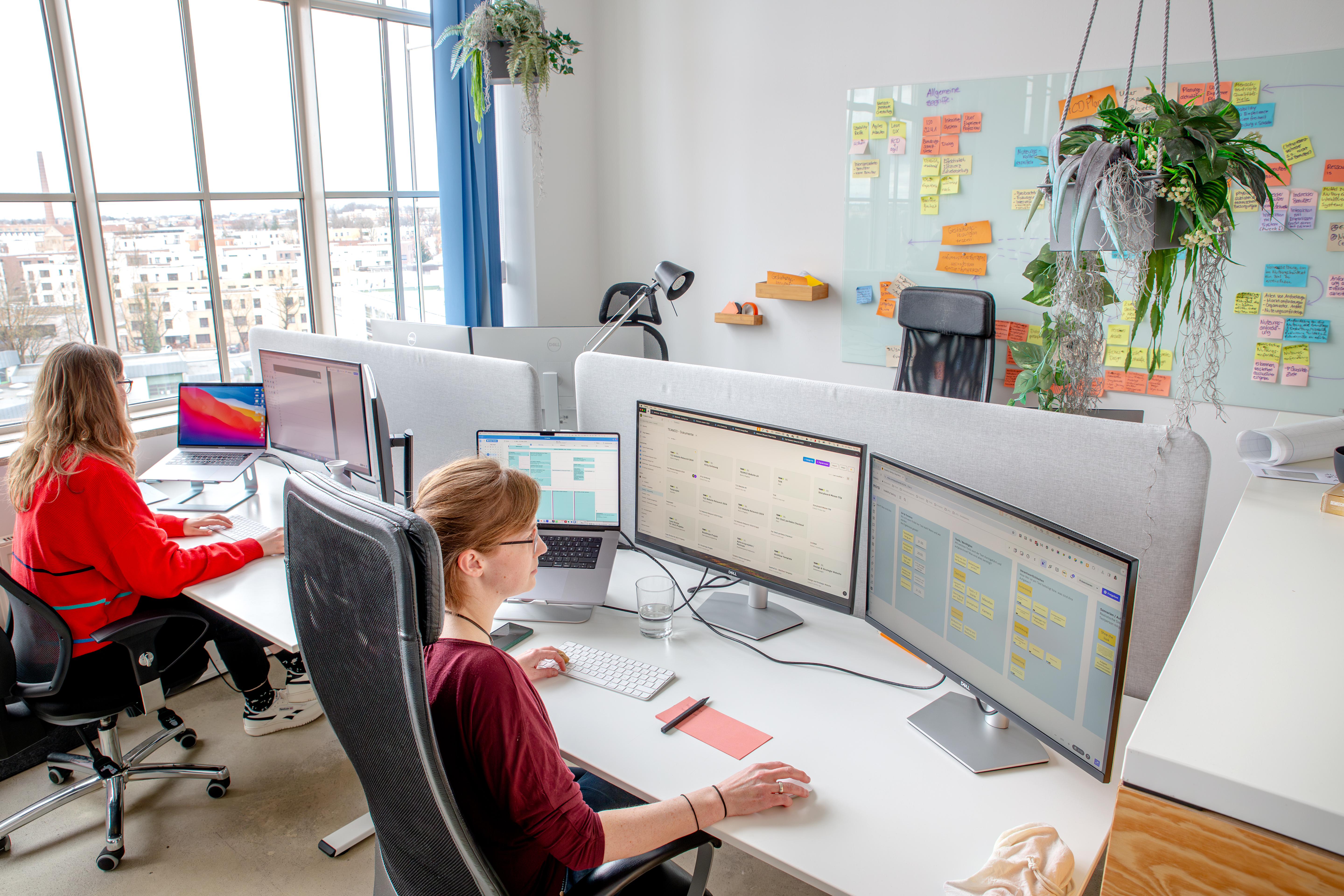 Zwei Designerinnen arbeiten konzentriert an ihren Laptops in einem großen, hellen Büro.